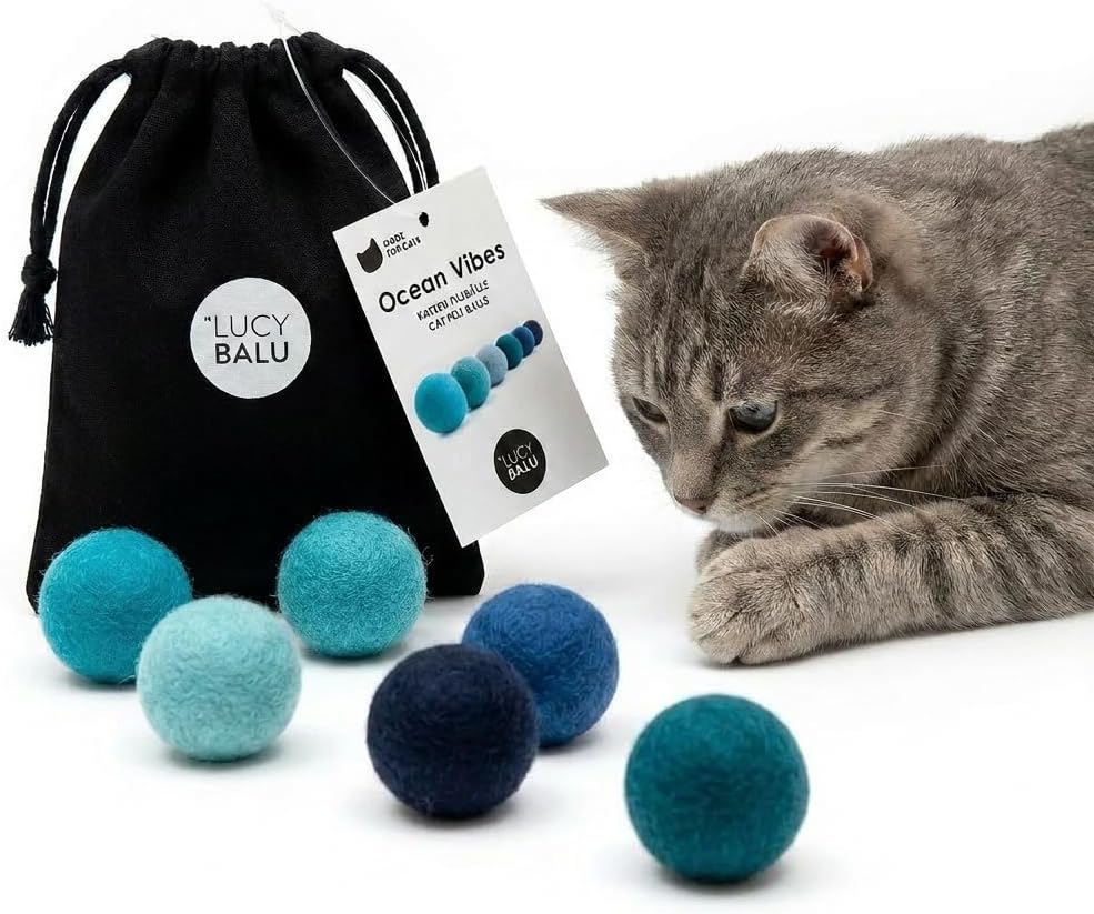 Un chat tigré jouant avec les balles en feutre bleu LucyBalu Ocean Vibes, accompagnées de leur pochon de rangement en coton noir.